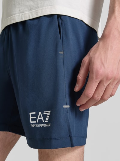 Männermodel trägt Shorts mit Logo und elastischem Bund von EA7 Emporio Armani, dunkelblauer Material-Mix mit Stretch-Anteil, Regular-Fit, Nahaufnahme Oberschenkel.