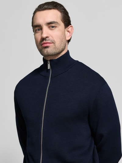 Männermodel trägt Relaxed Fit Strickjacke aus Viskose-Mix Modell 'TELLER' von SELECTED HOMME in Dunkelblau, Nahaufnahme Oberkörper. Feinstrick, Reißverschluss, Stehkragen, gerippte Abschlüsse, unifarben, langarm.