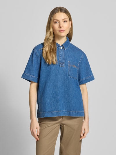 Frauenmodel trägt Regular Fit Jeansbluse aus reiner Baumwolle von Lacoste, tkanina stylizowana na denim, krój regular fit, kołnierzyk koszulowy, wyhaftowane logo, szwy w kontrastowym kolorze, krótka listwa guzikowa, krótki rękaw, wykończenie z bocznymi rozcięciami, brustasza, bawełna; Ganzkörperansicht von vorne
