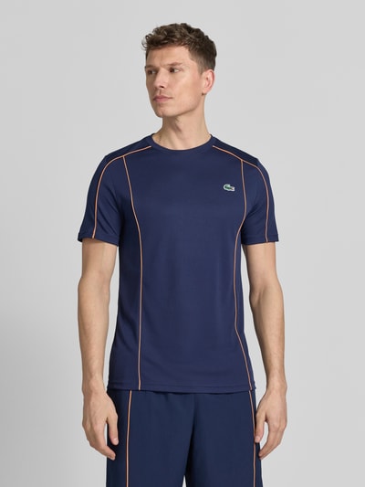 Männermodel trägt Regular Fit T-Shirt mit UV-Schutz 50+ von Lacoste Sport in Dunkelblau mit Kontraststreifen, Logo-Patch, Nahaufnahme Oberkörper