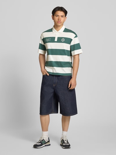 Męski model nosi Relaxed Fit Poloshirt aus reiner Baumwolle Modell 'DEVIN' von Only & Sons, zielono-białe szerokie pasy, kołnierzyk polo, krótki rękaw, dzianina, logo z przodu, całkowity widok z przodu