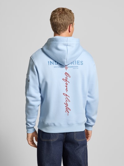 Männermodel trägt Hoodie mit Label-Details von Alpha Industries in Hellblau, Baumwoll-Mix, lockerem Schnitt, Ganzkörperansicht Rückansicht.
