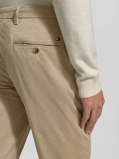 Männermodel trägt Slim Fit Chino aus Baumwoll-Mix Modell 'BLEECKER' von Tommy Hilfiger in Beige mit Label Patch, Detailaufnahme Rückansicht.