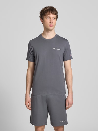 Männermodel trägt T-Shirt mit Label-Stitchings und Rundhalsausschnitt von CHAMPION in Grau, reine Baumwolle, Regular Fit, Ganzkörperansicht von vorne.