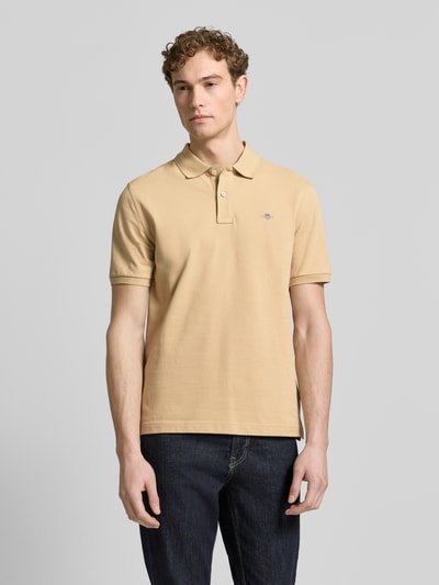 Männermodel trägt Slim Fit Poloshirt mit Logo-Stitching von Gant in Beige, reine Baumwolle, Polo-Kragen, Kurzarm, Ganzkörperansicht von vorne.