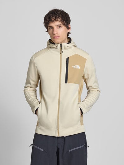 Männermodel trägt Funktionsjacke mit Napoleontasche Modell 'MOUNTAIN ATHLETICS' von The North Face in Beige mit Kapuze, Elastisch, Slim Fit, durchgehender Reißverschluss, Eingrifftaschen, Rückenlänge 70 cm, Ärmellänge 68 cm; Ganzkörperansicht von vorne.