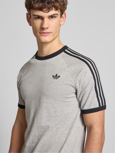 Männermodel trägt T-Shirt mit Label-Stitching von adidas Originals in Grau mit schwarzen Details, reine Baumwolle, Nahaufnahme Oberkörper
