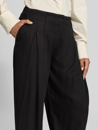 Frauenmodel trägt Wide Fit Jeans aus reinem Lyocell von Iro in Schwarz mit Bundfalten und Gesäßtaschen, Nahaufnahme Oberkörper.