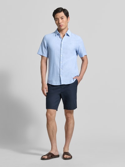 Männermodel draagt Slim Fit vrijetijdsoverhemd van mix van linnen en katoen model 'AKSEL' van Casual Friday in lichtblauw met korte mouwen, kentkraag, labelstitching en knoopsluiting, ruglengte maat M 78 cm, schouderbreedte 45 cm, mouwlengte 27 cm, gladde textuur en rechte vormen. Ganzkörperansicht von vorne.