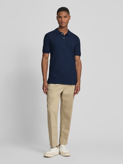 Männermodel trägt Slim Fit Poloshirt mit Label-Stitching von GAP aus Baumwoll-Elasthan-Mix in Dunkelblau, Ganzkörperansicht von vorne.