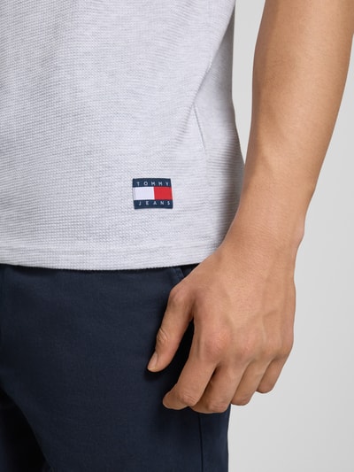 Männermodel trägt Regular Fit T-Shirt aus Baumwoll-Mix von Tommy Jeans in Hellgrau mit Logo-Stitching, Nahaufnahme Oberkörper.