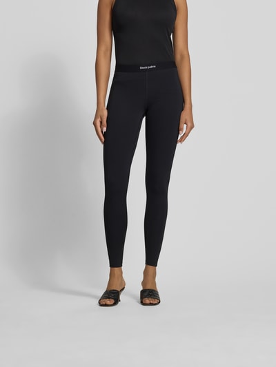 Frauenmodel trägt Leggings mit Label-Detail von black palms in Schwarz, Elastischer-Material-Mix, eng anliegende Passform, Knöchellänge, Elastischer-Bund, Ganzkörperansicht von vorne.