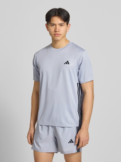 Männermodel trägt Regular Fit Sport T-Shirt mit Logo-Print von adidas Training in Hellgrau, Kurzarm, Mock-Eyelet-Gewebe, Ganzkörperansicht von vorne.