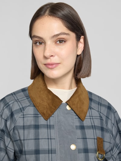 Frauenmodel trägt Regular Fit Jacke aus reiner Baumwolle Modell 'CARNFORTH' von Barbour, wzór w kratę, cordowe obszycie, wyhaftowane logo, detal z pierścieniem, kolor szary, tekstura gładka, Nahaufnahme Oberkörper.