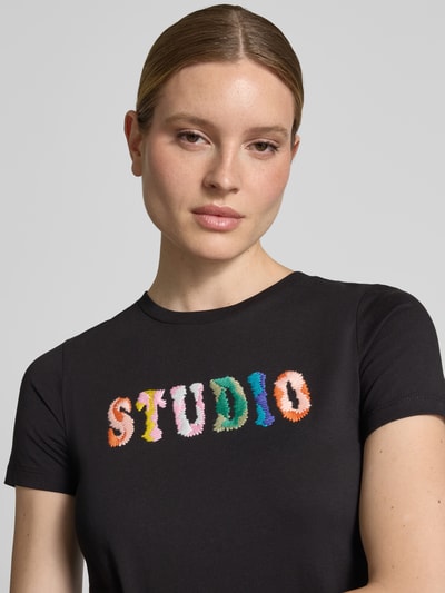 Frauenmodel trägt Regular Fit T-Shirt mit Logo-Stitching von JAKE*S STUDIO WOMAN, reine Baumwolle, schwarzer Stoff, bunte Buchstaben, Nahaufnahme Oberkörper.