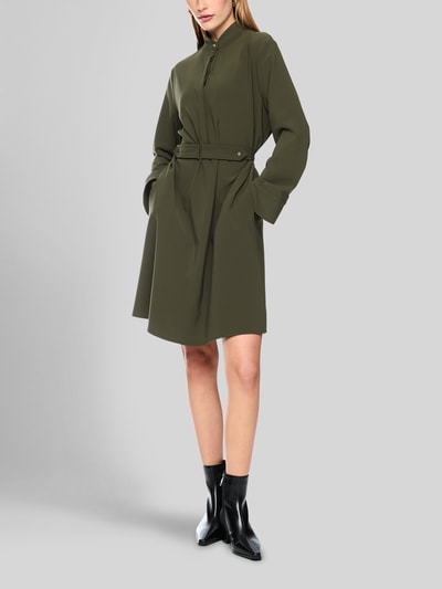 Frauenmodel trägt Knielanges Kleid mit Stehkragen und Gürtel von Marc Cain in Olive, taillierter Schnitt, Material-Mix, Ganzkörperansicht von vorne.