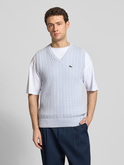 Männermodel trägt Regular Fit Pullunder aus Baumwoll-Mix von Lacoste in Hellblau, Zopfmuster, Strickoptik, Logo-Detail, Ganzkörperansicht von vorne.