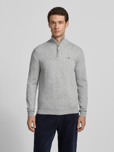 Männermodel trägt Pullover aus reiner Wolle von GANT in Hellgrau, Feinstrick, Troyerkragen mit Reißverschluss, Ganzkörperansicht von vorne.