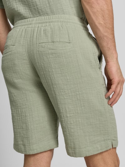 Mężczyzna nosi Shorts mit Eingrifftaschen und elastischem Bund od Lindbergh z bawełny, kolor jasna zieleń, tekstura marszczona, krój loose fit, tylne kieszenie, szerokość w rozmiarze M 43 cm, długość nogawki 22 cm, całkowity widok z tyłu