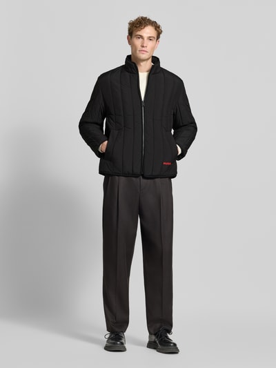 Männermodel trägt schwarze Regular Fit Steppjacke Modell 'Brenoto2611' von HUGO, lockere Passform, Ganzkörperansicht von vorne, Herren Steppjacke von HUGO.