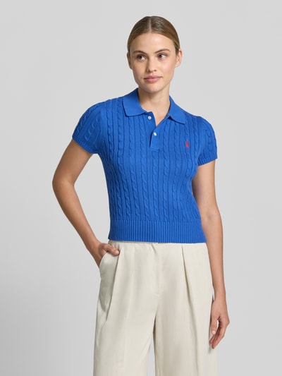Modelka nosi Regular Fit Strick-Poloshirt aus reiner Baumwolle von Polo Ralph Lauren, efekt: jednolity kolor, krój regular fit, wzór: ścieg warkoczowy, wyhaftowane logo, kołnierzyk polo, rękaw: krótki rękaw, zakończenie: prążkowane, dzianina, czysta bawełna, całkowity widok z przodu.