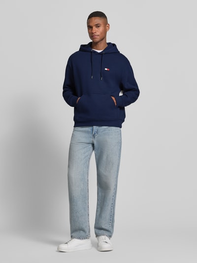 Männermodel trägt Regular Fit Hoodie aus reiner Baumwolle von Tommy Hilfiger, Optik: Unifarben, Logo-Applikation, Kängurutasche, Materialverarbeitung: Sweat, Ganzkörperansicht von vorne.