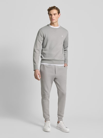 Mężczyzna nosi Sweatshirt mit Label-Stitching od Polo Ralph Lauren, bawełniany miks, krój regular fit, jasnoszary kolor, cała sylwetka z przodu.
