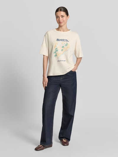 Frauenmodel trägt T-Shirt mit Motiv-Print und Rundhalsausschnitt von Jake*s Casual in Beige, lockerer Schnitt, reine Baumwolle, Motiv in Pastellfarben, dunkle Jeans, Ganzkörperansicht von vorne.