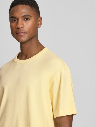Männermodel trägt Cropped T-Shirt mit Rundhalsausschnitt von GAP in hellem Gelb, reine Baumwolle, glatte Textur, Nahaufnahme Oberkörper.