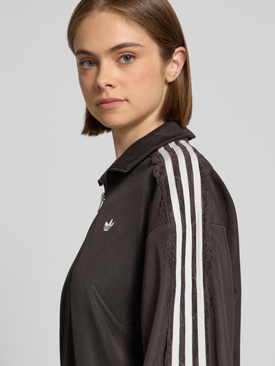 Kobiece model prezentuje Oversized Sweatjacke aus Baumwoll-Mix model 'LACE OVERSIZED' od adidas Originals w kolorze czarnym z białymi paskami, zbliżenie na górną część ciała