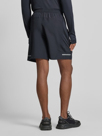 Męski model nosi Tech Utility Shorts mit Label-Print von Under Armour, prosty krój, elastyczny pas, styl utility, nadruk z logo, szerokość w rozmiarze M: 37 cm, długość wewnętrzna nogawki w rozmiarze M: 22 cm, widok całej sylwetki z tyłu.