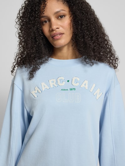 Frauenmodel trägt Relaxed Fit Sweatshirt mit Logo-Detail von Marc Cain, hellblauer Baumwoll-Mix, Rundhalsausschnitt, Nahaufnahme Oberkörper.