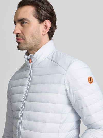 Männermodel trägt Steppjacke mit Zweiwegereißverschluss Modell 'Alexander' von SAVE THE DUCK in Stepp-Optik, Nahaufnahme Oberkörper, Regular Fit, hellgraue Farbe, glatte Textur, Sichtbarkeit des Markenlogos.