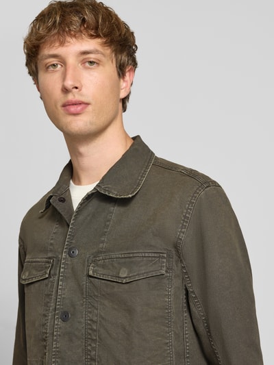 Männermodel trägt Slim Fit Jeansjacke aus reiner Baumwolle von G-Star RAW in Olive, sichtbare Knopfleiste, Nahaufnahme Oberkörper.