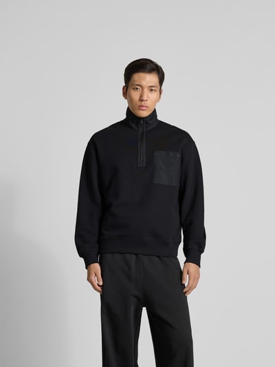 Mannenmodel draagt Troyer aus reiner Baumwolle van MAISON KITSUNÉ, regular fit, schipperskraag, labeldetail, borstzak, kleur zwart, ruglengte bij maat M 68 cm, volledige vooraanzicht.