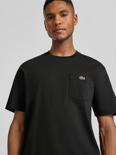 Männermodel trägt Regular Fit T-Shirt aus reiner Baumwolle von Lacoste, unifarben schwarz mit Logo-Stitching, Nahaufnahme Oberkörper.
