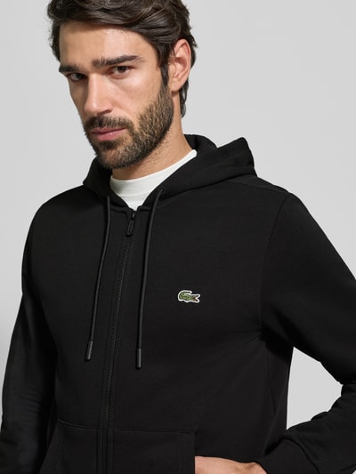 Männermodel trägt Sweatjacke mit Reißverschluss von LACOSTE aus schwarzem Baumwoll-Mix mit Kapuze, Label-Detail, Eingrifftaschen, Regular-Fit, Nahaufnahme Oberkörper.