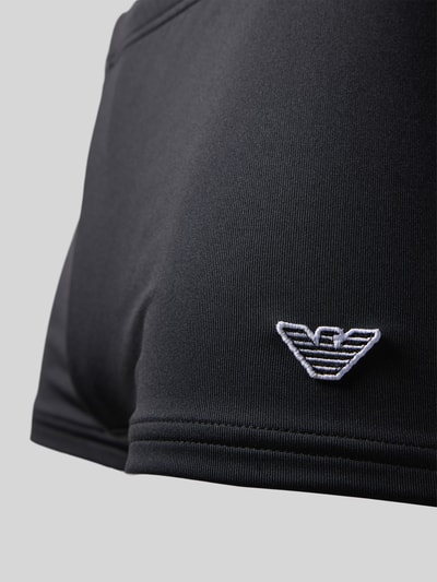 Männermodel trägt Badehose mit Label-Patch von Emporio Armani, schwarze Stretchoptik, Trunk Fit, Nahaufnahme Oberkörper.