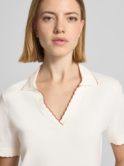 Kobiece model prezentuje Slim Fit Poloshirt mit Wellensaum und V-Ausschnitt von Marc Cain, mieszanka bawełny i elastanu, krój slim fit, dekolt w serek, falisty brzeg, długość tyłu w rozmiarze 36: 58 cm, zbliżenie na górną część ciała.