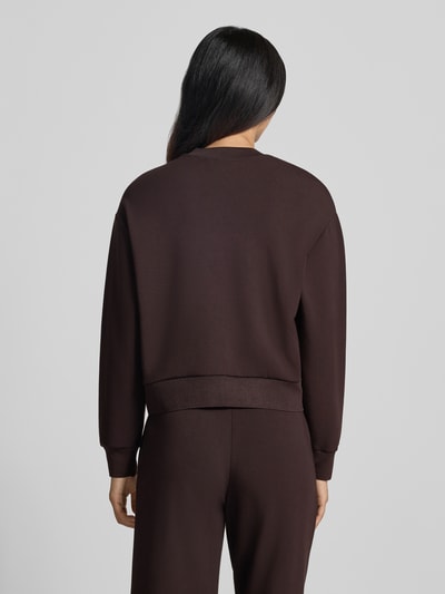 Frauenmodel trägt Sweatjacke mit Label-Print von Armani Exchange in Dunkelbraun, lockere Passform, glatte Textur, Ganzkörperansicht Rückansicht. Damen Sweatjacke von Armani Exchange, Viskose-Mix mit Stretch-Anteil, Zweiwege-Reißverschluss, seitliche Eingrifftaschen.
