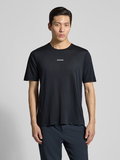 Männermodel trägt T-Shirt mit Rundhalsausschnitt und Logo von Salomon in Schwarz, Regular-Fit, Rückenlänge 69 cm bei Größe M, Ganzkörperansicht von vorne