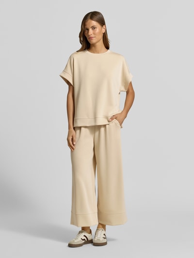 Frauenmodel trägt Wide Leg Sweatpants aus Modal-Mix von Rich & Royal in Beige mit elastischem Bund, Bundfalten und Taschen, Ganzkörperansicht von vorne.