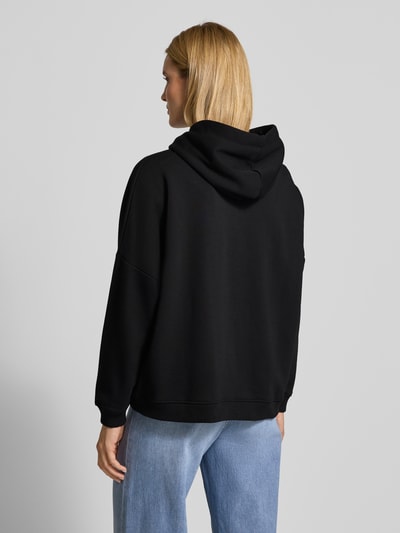 Frauenmodel trägt Oversized Hoodie mit Kapuze von miss goodlife in Schwarz aus Baumwolle mit Tunnelzug, Label-Detail, gerippten Abschlüssen, Ganzkörperansicht Rückansicht