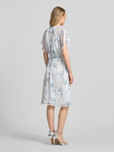 Frauenmodel trägt Knielanges Kleid mit Serafino-Kragen von More & More aus Chiffon mit Schmetterlingsärmel und Bindegürtel, Rückansicht Ganzkörperansicht.