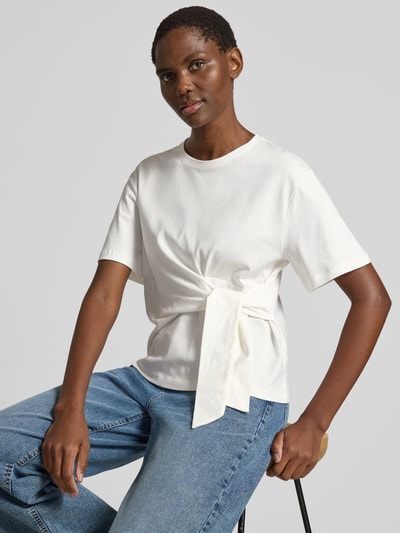 Frauenmodel trägt T-Shirt mit Knoten-Detail und Rundhalsausschnitt von Christian Berg Woman aus Reine Baumwolle, Regular-Fit, Rückenlänge 55 cm bei Größe S, in Weiß mit glatter Textur und schlichten Formen, Nahaufnahme Oberkörper.