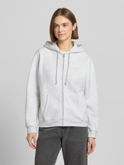 Vrouwenmodel draagt Sweatjacke mit Kapuze van Levi's®, lichtgrijze katoenmix, losse pasvorm, capuchon, rits, steekzakken, labeldetail, ribboorden. Ganzkörperansicht van voren.