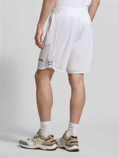 Männermodel trägt Relaxed Fit Sport-Shorts mit Logo-Print Modell 'SH_TOC SPIN 9 INCH' von BOSS Green, Optik: Unifarben, Kontraststreifen, Beinabschluss elastisch, seitliche Eingrifftaschen, Ganzkörperansicht Rückansicht.