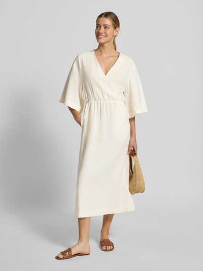 Frauenmodel trägt Midikleid aus Leinen-Mix mit Kimonoärmeln Modell 'Laura' von GUIDO MARIA KRETSCHMER WOMAN in Creme, Ganzkörperansicht von vorne. Taillierter Schnitt, V-Ausschnitt, Wickel-Optik, strukturierte Oberfläche.