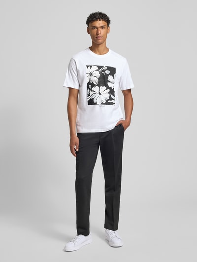 Männermodel trägt Herren T-Shirt mit Motiv-Print Modell 'LUCAS' von Jack & Jones Premium aus reiner Baumwolle, Slim-Fit, Rundhalsausschnitt, Rückenlänge bei Größe M 67 cm, weiße und schwarze Farbtöne, glatte Textur, Ganzkörperansicht von vorne.