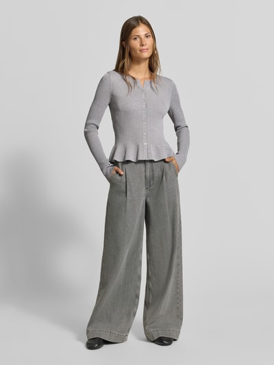 Frauenmodel trägt Strickjacke aus Viskose-Mix von MYON, graue Ripp-Optik, rund, tailliert, Rüschenbund, Ganzkörperansicht von vorne.